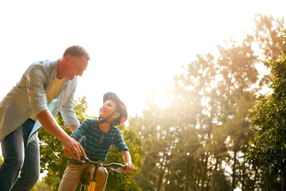 Person helping a child ride a bike with scenic background